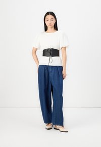 Hvit ribbestrikket topp med pufferm, kombinert med et svart bredt belte med snøring over løse denimbukser og beige leiligheter.