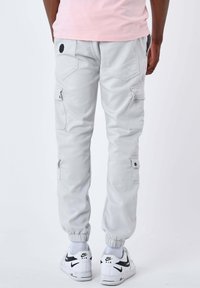 Uomo che indossa pantaloni cargo jogger grigio chiaro e sneakers Nike Air bianche, mostrato di schiena su uno sfondo neutro.
