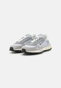 Világosszürke sneaker, szintetikus és velúr anyagból, texturált részletekkel, fekete gumitalppal és fehér fűzővel. Jellemzője a logó részlet.
