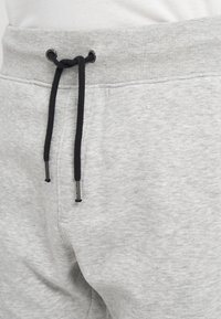 Hellgraue Jogginghosen mit geripptem Bund und schwarzem Kordelzug, vorne zu einem einfachen Knoten gebunden.