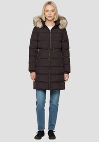 Zwarte donsjas met een capuchon met bontvoering, horizontale doorgestikte structuur, ritssluiting aan de voorkant, getailleerde taille en zijzakken. Gecombineerd met een blauwe spijkerbroek.