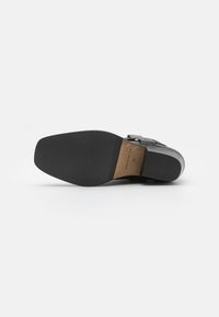 Zapato de cuero negro con una textura suave, presenta una puntera redondeada, una plantilla de madera y una suela de goma plana para tracción.