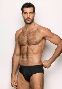 Slip neri indossati da un uomo con un fisico muscoloso, caratterizzati da una superficie liscia e una fascia elastica in vita, esposti su uno sfondo chiaro.