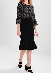 Black fitted skirt with flared hem. Partnered with a floral patterned long-sleeve top. Black block-heeled shoes with ankle straps.