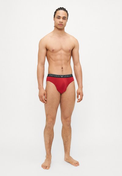 Caleçons en coton rouges avec une taille élastique noire portant l'inscription "Emporio Armani". Le design présente une coupe ajustée et une texture lisse.