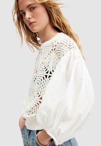 Suéter blanco con un diseño texturizado de punto en la parte delantera y mangas abullonadas. La parte trasera y las mangas están hechas de algodón suave.