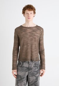 Brun tekstureret langærmet skjorte med vandrette striber, parret med grå camouflerede jeans med en afslappet pasform og lommer.