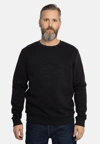 Sudadera negra con cuello redondo y mangas largas. Presenta un logo elevado y en relieve en la parte frontal, así como puños y dobladillo acanalados.