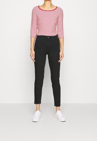 Rot-weiß gestreiftes Langarmoberteil, kombiniert mit hochtaillierten schwarzen Jeans und weißen Sneakers, mit Knopfleiste und schmaler Passform.