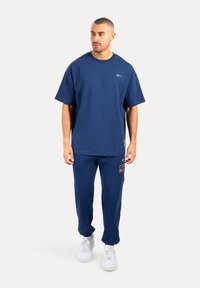 Camiseta de manga corta azul marino con cuello redondo, combinada con joggers azul marino a juego; incluye un pequeño logo y detalle de parche.
