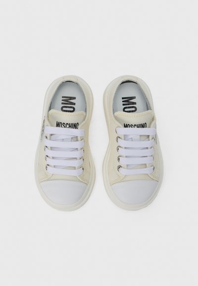 Λευκά πάνινα sneakers με καουτσούκ προστατευτικό στην μύτη, με λευκά κορδόνια και λογότυπο «MOSCHINO» στη γλώσσα και στις εσωτερικές σόλες.