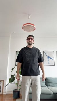 Črna oversize majica s sprednjim bleščečim dizajnom, v kombinaciji s svetlimi cargo hlačami. Dodatki vključujejo sončna očala in črno kapo.
