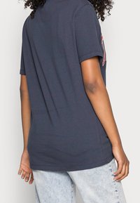 Navy cotton t-shirt with short sleeves, a relaxed fit, and a straight hem. Worn with light-wash denim jeans. Minimalistic design, no visible graphics.