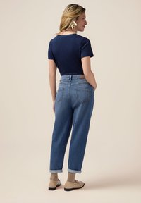 Top de manga corta azul marino combinado con unos vaqueros de mezclilla clara y holgados; puños doblados; zapatos elegantes; cabello peinado a un lado; accesorios mínimos.