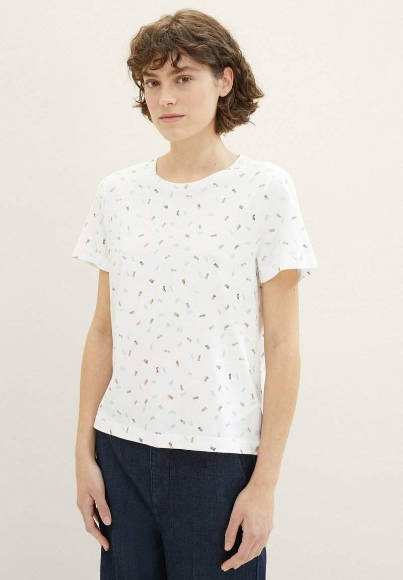 T-shirt blanc à manches courtes en coton, présentant un motif géométrique multicolore avec de petites formes et un col rond.