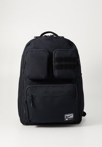 Sac à dos noir avec plusieurs poches zippées, tissu texturé, bretelles rembourrées et accents en Velcro. Présente un logo de la marque en bas à l'avant.