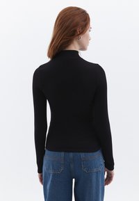 Zwarte longsleeve top met een getailleerd ontwerp, hoge kraag en ribbelstructuur, gecombineerd met high-waisted denimjeans met achterzakken.