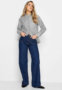 Chemise à rayures avec poche poitrine, associée à un jean en denim bleu foncé à taille haute et jambes larges. Tissu lisse et coupe ajustée.