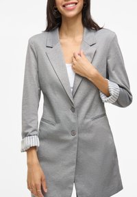 Blazer grigio con rever a notched, due bottoni e tasche laterali; le maniche presentano un risvolto con righe blu e bianche.