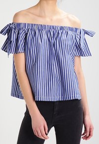Niebiesko-biała, paskowana bluzka typu off-the-shoulder z falbanami na rękawach i troczkami, wykonana z lekkiego materiału, luźny krój.