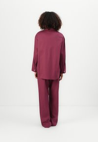 Burgundy tvådelat set bestående av en löst sittande långärmad skjorta och matchande vida byxor, tillverkad av ett texturerat bomullstyg.