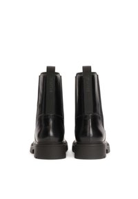 Botas de tobillo de cuero negro con paneles elásticos laterales, una pestaña en el bucle para facilitar su uso y una suela de goma gruesa. Acabado suave, diseño minimalista.