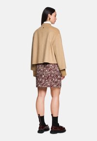 Beige cropped jacket made of wool, paired with a burgundy floral patterned skirt. Model wears dark glossy ankle boots with black socks.