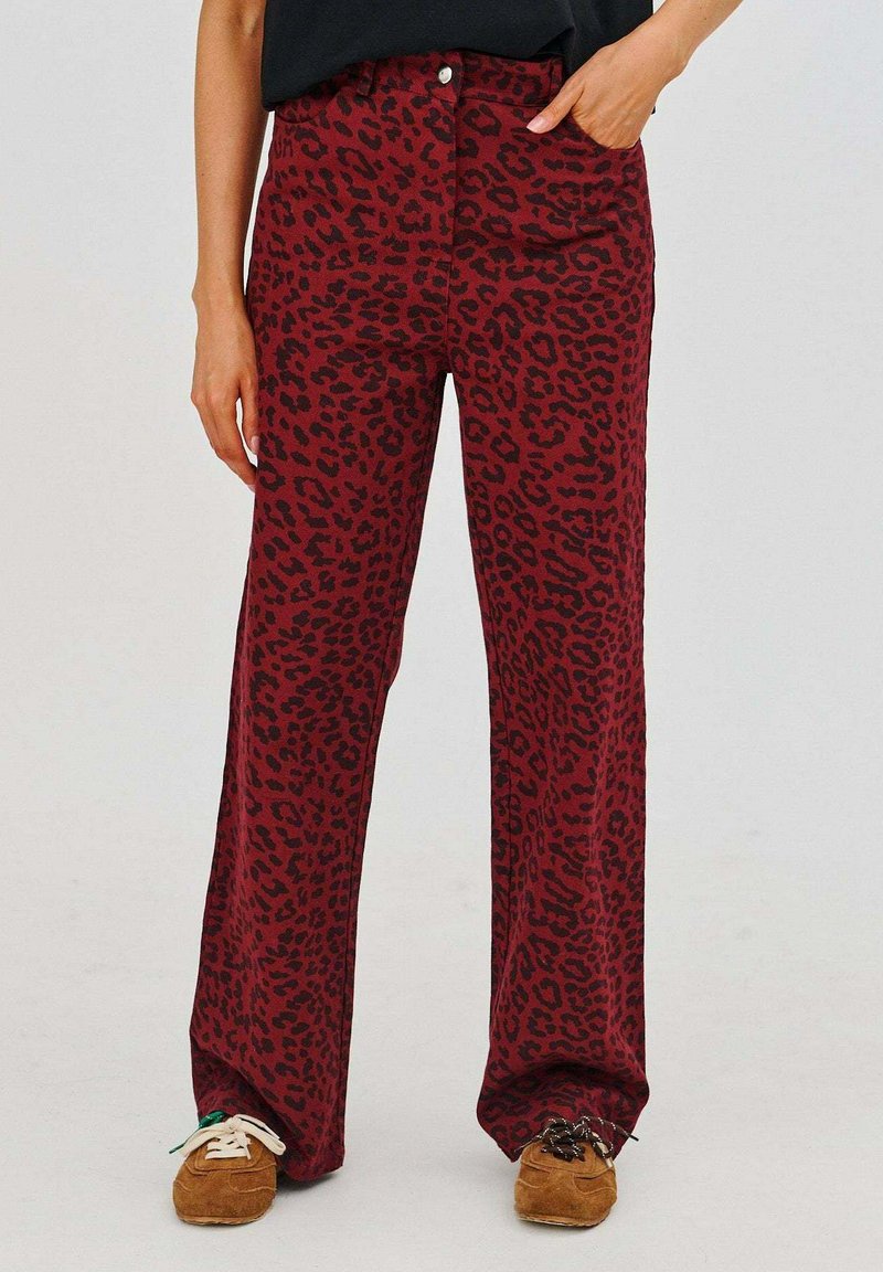 Červené nohavice so zvieracím potlačou z mäkkej tkaniny, s vysokým pásom, rovnými nohavicami a prednými vreckami, skombinované s hnedými topánkami.