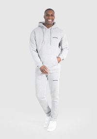 Grauer Pullover und passende Jogginghose mit "SMILODOX"-Logo. Hergestellt aus weichem Stoff, mit Kapuze und Taschen. Weiße Sneakers runden das Outfit ab.
