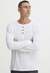 Witte lange mouwen henley shirt van textuurstof, met een ronde halslijn en drie zwarte knopen op de borst.
