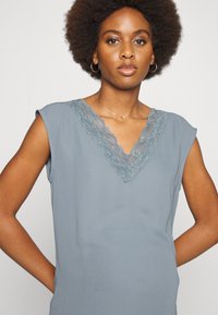 Top cinza sem mangas com decote em V, apresentando um delicado acabamento em renda. Tecido suave com uma textura macia, ideal para uso casual.