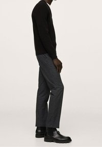 Zwarte geribde trui, grijze ruitbroek en zwarte chelsea boots, zijaanzicht, dat de textuur en pasvorm van de kleding benadrukt.