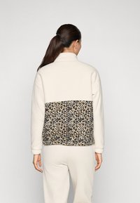 Fleecejacke mit einer cremefarbenen Vorderseite und einem Rückenpaneel im Leopardenmuster. Weicher Stoff mit hohem Kragen und gerippten Bündchen.