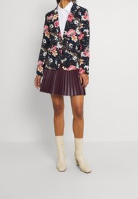 Sako s květinovým vzorem v námořnické modři s růžovými a bílými květy, v kombinaci s plisovanou švestkovou sukní a lesklými krémovými kotníkovými botami.