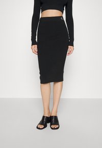 Černá žebrovaná midi sukně s elastickým pasem, spárovaná s odpovídajícím crop topem s dlouhým rukávem. Boty jsou černé nazouvací muly s blokovým podpatkem.