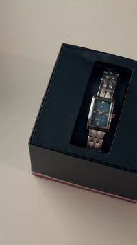 Zilveren horloge van roestvrij staal met een rechthoekige wijzerplaat, blauwe wijzerplaat, zilveren accenten en een patroonband, weergegeven in een zwarte doos.