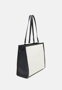 Svart och vit tote-väska med en strukturerad form. Har en slät svart läderbas och remmar samt en texturerad vit kanvasfront.