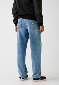 Jasnoniebieskie dżinsy z denimu o luźnym kroju, z tylnymi kieszeniami i naszywką z logo, zestawione z czarnymi tenisówkami. Gładka faktura.