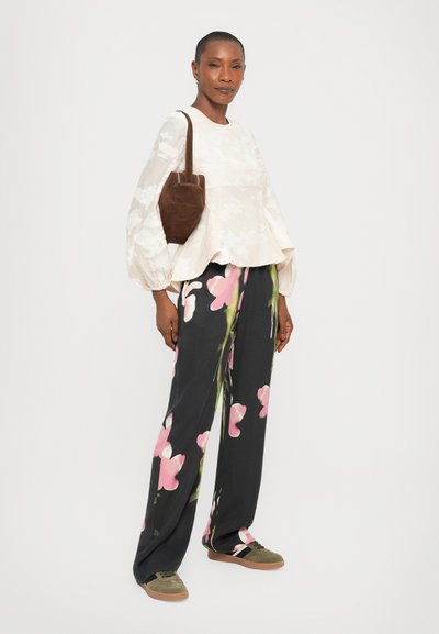 Witte blouse met bloemenpatroon en pofmouwtjes, gecombineerd met zwarte wijde broek met roze bloemen. Bruine suède handtas en groene sneakers.