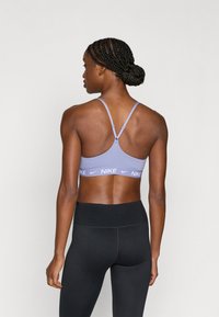 Ανοιχτόμωβ αθλητικό σουτιέν με ρυθμιζόμενους ιμάντες και λευκή λωρίδα με το λογότυπο της Nike. Λείο υλικό με σχεδίαση racerback. Μαύρο ψηλόμεσο κολάν.