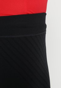 Close-up of black ribbed high-waist waistband paired with red fabric, highlighting garment textures and stitching detail.