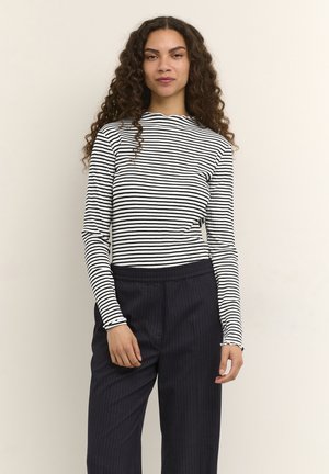 Schwarz-weiß gestreiftes Langarmoberteil mit Stehkragen und gerafften Bündchen, kombiniert mit dunklen, fein gestreiften Hosen. Glatte Stofftextur.