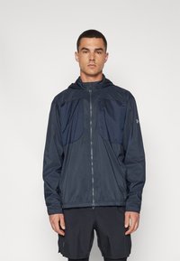 Veste coupe-vent marine avec fermeture éclair et capuche. Dotée d'un panneau supérieur texturé et de poignets élastiques, fabriquée en matériau léger et résistant à l'eau.