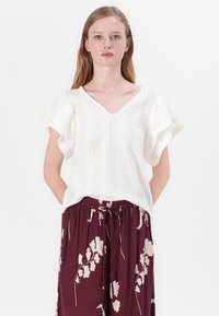 Hvit V-hals bluse med volangkortermede, med teksturerte striper. Kombinert med burgunder brede bukser prydet med lyse blomster mønstre.