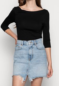Black long-sleeve top with a boat neck, paired with a distressed light blue denim skirt featuring a front slit and frayed hem.