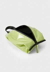Saco impermeável verde com acabamento brilhante, fecho em zip e realces em preto. Apresenta uma pega robusta para facilitar o transporte. Forma compacta e triangular.