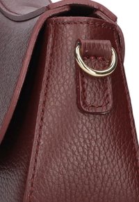 Bordeaux leren handtasdetail, met een gestructureerd oppervlak, goudkleurige hardware en een versterkte band met een gestikte accent.