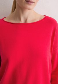 Pulli mit weitem, abgerundetem Ausschnitt, aus weichem, lebhaftem pinkfarbenem Stoff; bietet einen lockeren Sitz und lange Ärmel.