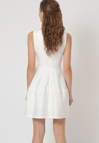 Vestido blanco sin mangas con un cuerpo ajustado, falda acampanada y una sutil textura. Presenta una costura en la parte posterior y un dobladillo limpio. Tejido ligero.