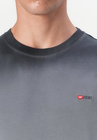 Šedé bavlnené tričko s okrúhlym výstrihom. Obsahuje malé červenobiele logo Diesel na ľavej hrudi. Hladká textúra a priliehavý dizajn.